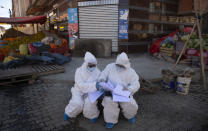 Healthcare workers dressed in full protective gear organize their documents of data they have collected during a house-to-house new coronavirus testing drive, ringed by a produce market in the Villa Dolores neighborhood of El Alto, Bolivia, Saturday, July 18, 2020. (AP Photo/Juan Karita)