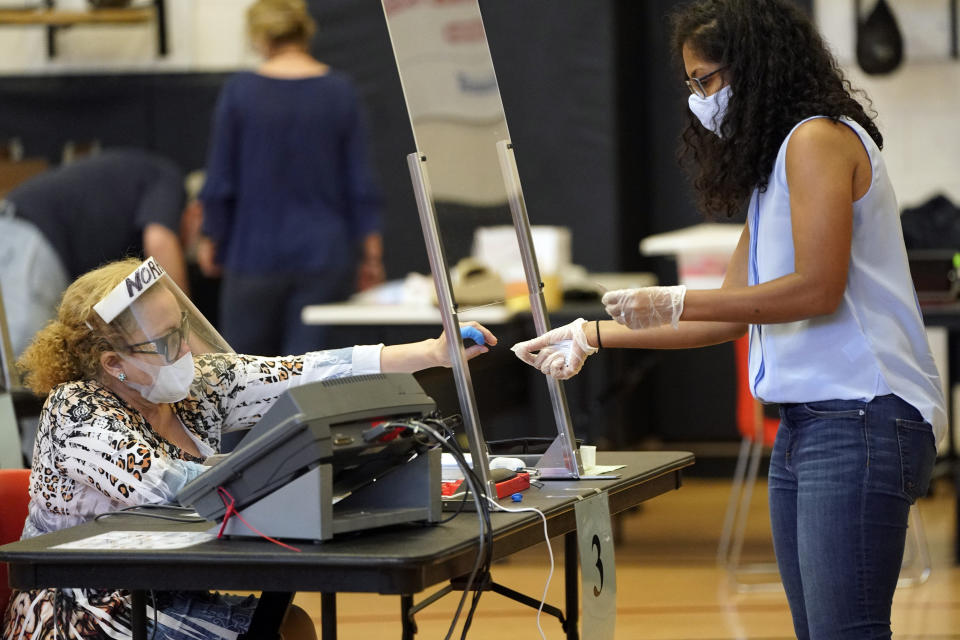 Harris County election clerk Nora Martinez, left, helps a voter, Monday, June 29, 2020, in Houston. Early voting for the Texas primary runoffs began Monday. (AP Photo/David J. Phillip)
