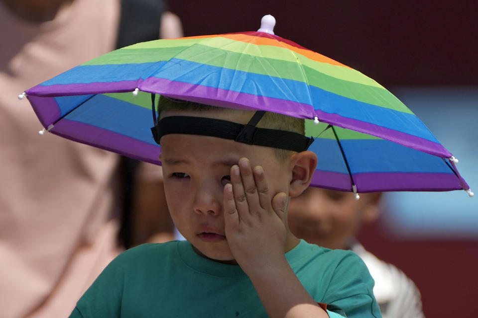 A boy wearing a rainbow umbrella wipes his sweat as he visits the Forbidden City on a sweltering day in Beijing, Friday, July 7, 2023. Earth's average temperature set a new unofficial record high on Thursday, the third such milestone in a week that already rated as the hottest on record. (AP Photo/Andy Wong)