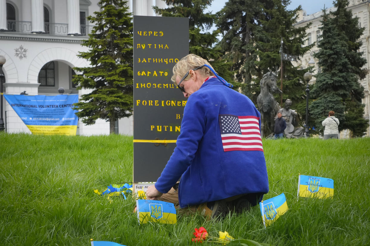 Routh kneels in the grass next to a sign written with Cyrillic alphabet.