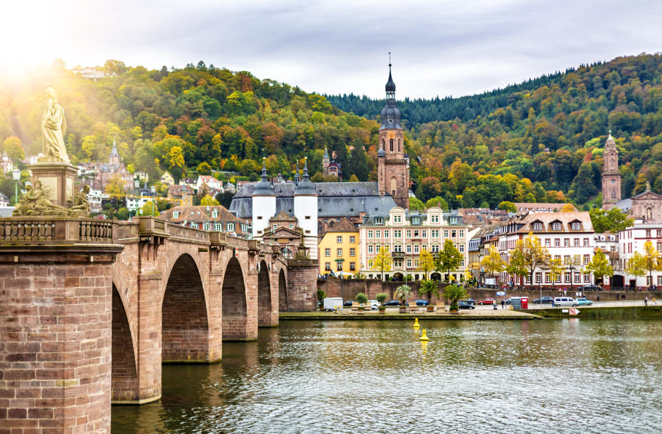 Historic bridge over river with old European buildings and a hill in the background. Statue on left