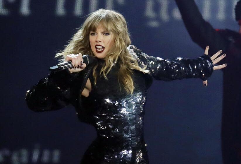 A woman in a shiny black outfit sings into a microphone while on stage