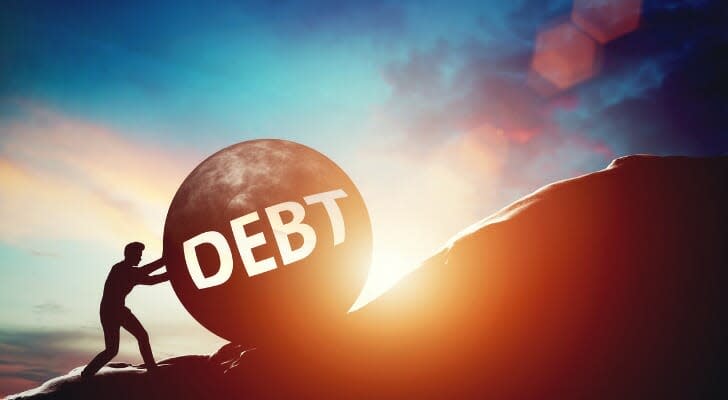 Man pushing a large ball labeled "DEBT" up a steep hill