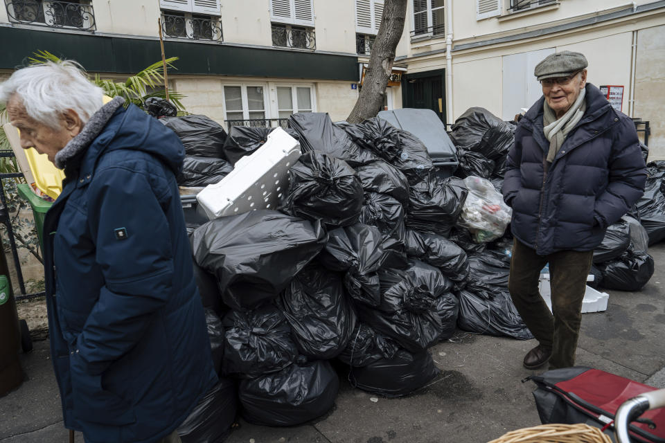 People walk past piles of garbage in Paris, Monday, March 13, 2023. A contentious bill that would raise the retirement age in France from 62 to 64 got a push forward with the Senate's adoption of the measure amid strikes, protests and uncollected garbage piling higher by the day. (AP Photo/Lewis Joly)