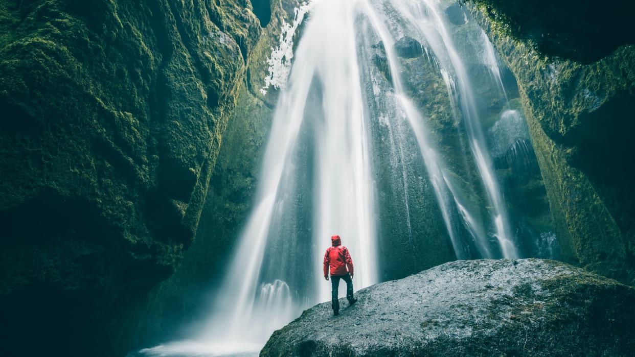  A man stands on a rock in front of a cascading waterfall in Iceland. 