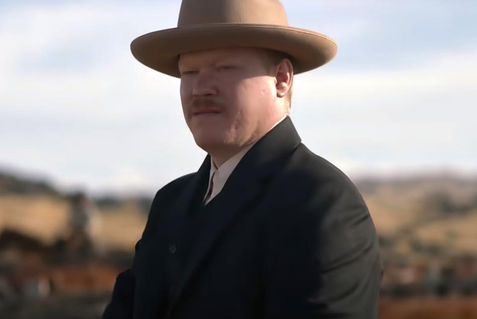 Jesse wears a flat brim hat in front of a country background