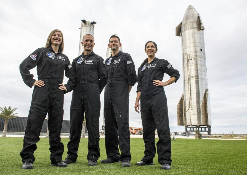 Two men and two women, dressed in black overalls, stand together on a grassy field.