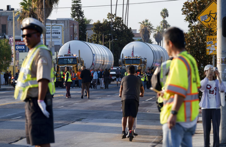 Traffic enforcement officers clear the way as trucks haul two rocket motors slowly down Figueroa Street in Los Angeles, Wednesday Oct. 11, 2023. The giant rocket motors, required to display the retired NASA space shuttle Endeavour as if it’s about to blast off, were trucked over two days from Mojave Air and Space Port to LA’s Exposition Park. (AP Photo/Richard Vogel)