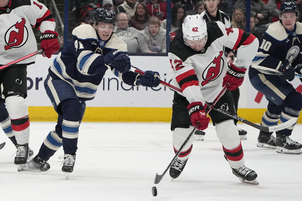 New Jersey Devils center Curtis Lazar (42) reaches for the puck in front of Columbus Blue Jackets center Kent Johnson (91) in the first period of an NHL hockey game Friday, Jan. 19, 2024, in Columbus, Ohio. (AP Photo/Sue Ogrocki)