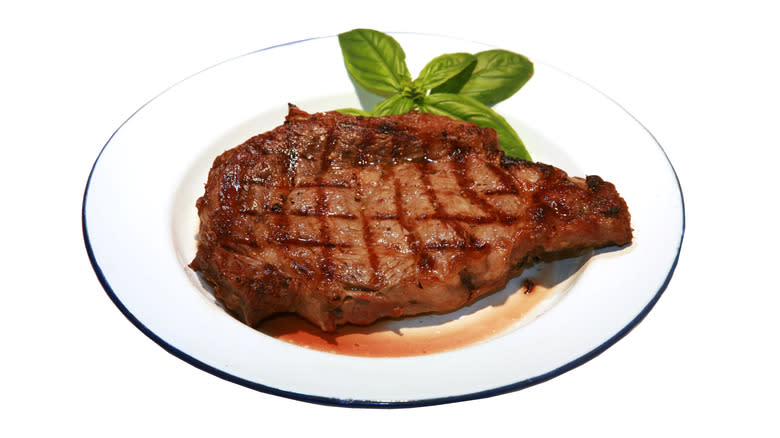 Grilled steak on white plate with basil