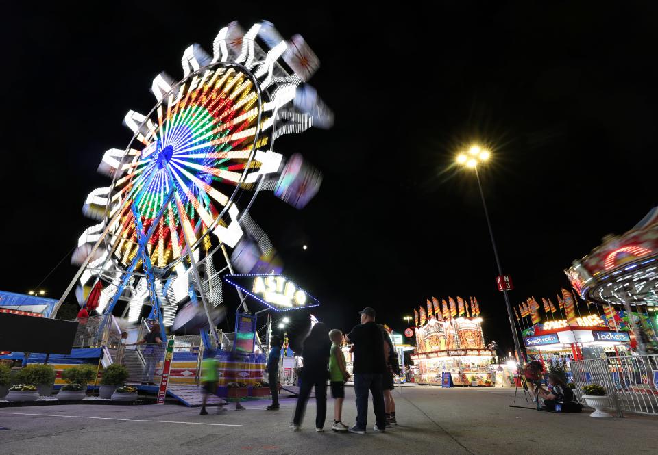 Fair-goers watch the glow of the ferris wheel on the first night of the Kentucky State Fair at the Kentucky Exposition Center in Louisville, Ky. on Aug. 19 2021.  