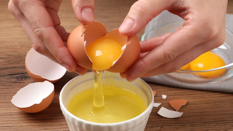 Hands separating an egg yolk into a dish
