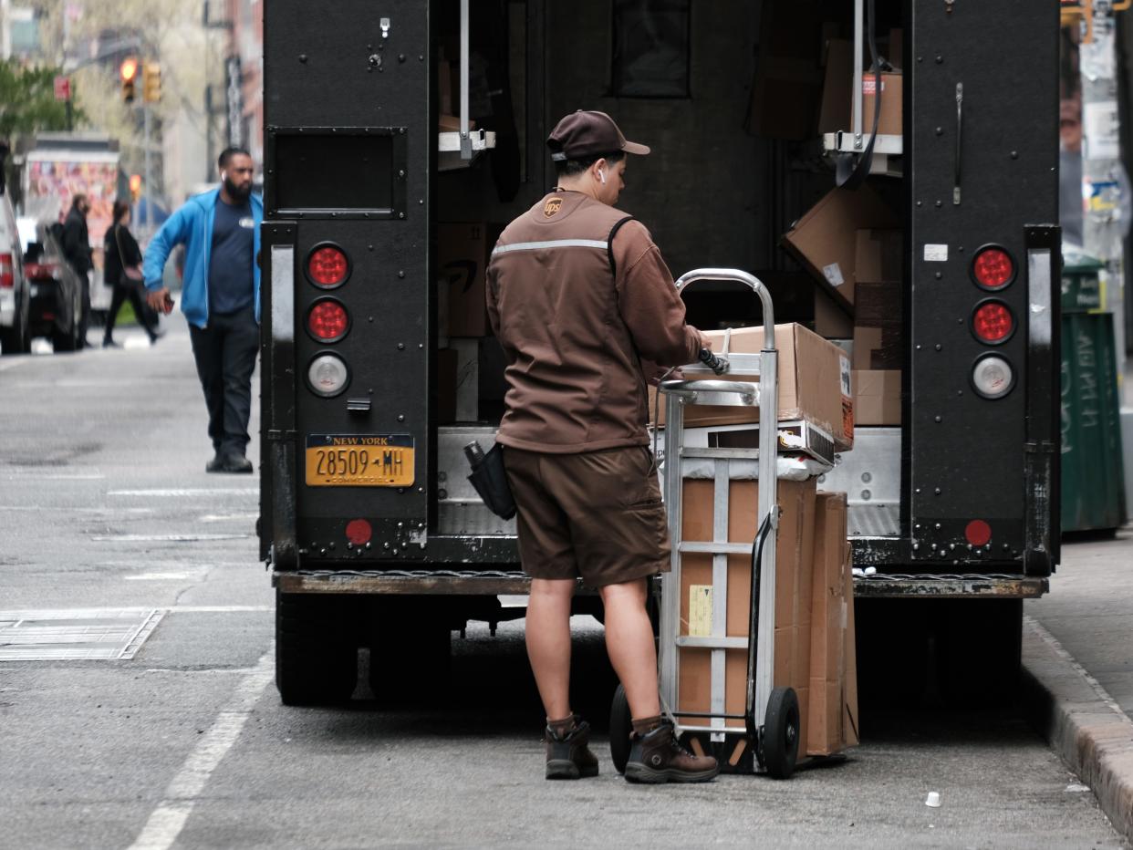 UPS driver stands behind his truck with packages on a dolly.