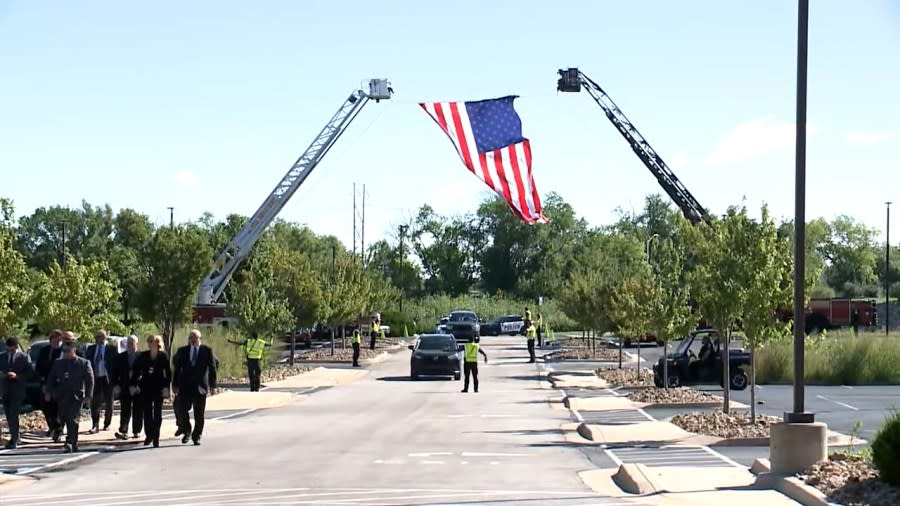 Crews hold an American flag over the entrance to the funeral for fallen Fairway Officer Jonah Oswald on Aug. 14, 2023.