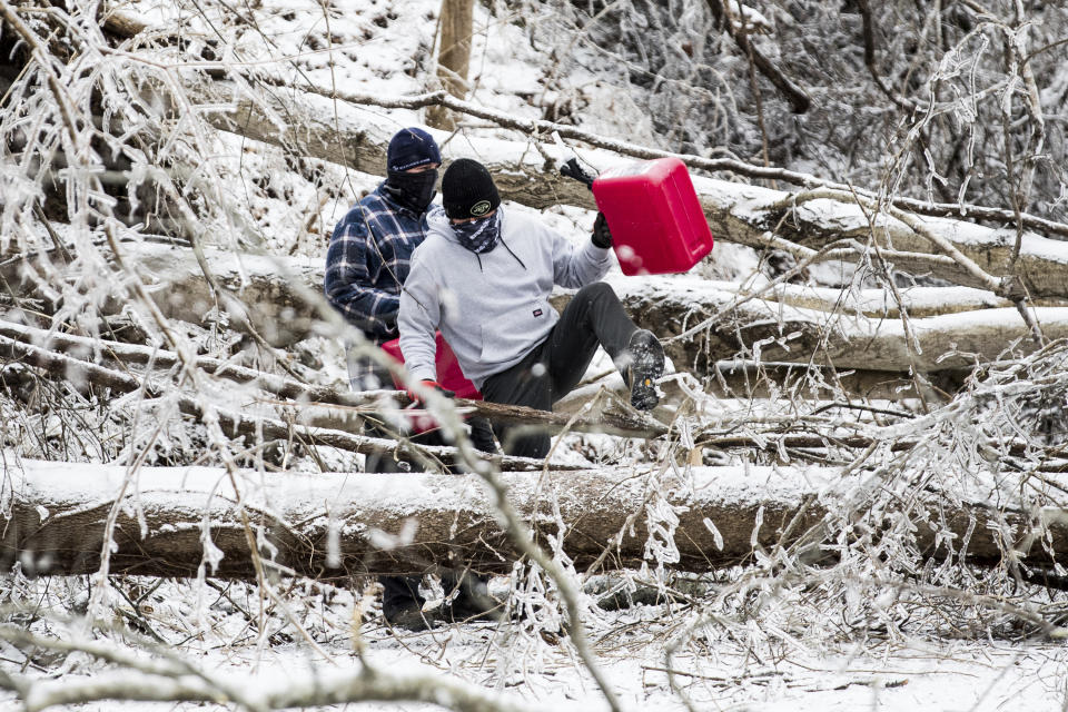 Two men climb over downed trees as they head out to retrieve gas for generators, Tuesday, Feb. 16, 2021, in Huntington, W.Va., following a winter weather system. (Sholten Singer/The Herald-Dispatch via AP)