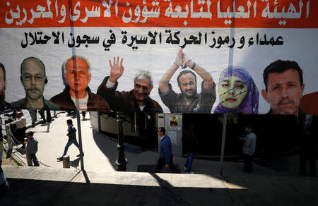 People walk past a poster depicting Palestinian prisoners held in Israeli jails, in the West Bank city of Ramallah April 17, 2017. REUTERS/Mohamad Torokman