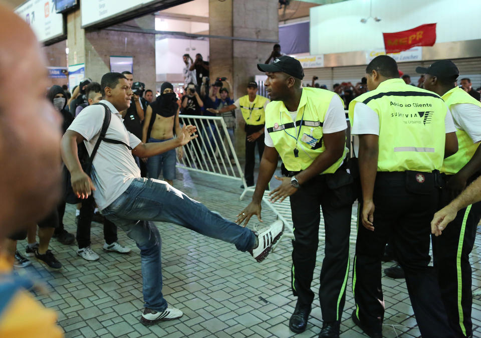 A demonstrators kicks a security guard during a protest against the increase of bus fares in Rio de Janeiro, Brazil, Thursday, Feb. 6, 2014. Last year, millions of people took to the streets across Brazil complaining of higher bus fares, poor public services and corruption, while the country spends billions on the World Cup, which is scheduled to start in June. (AP Photo/Leo Correa)
