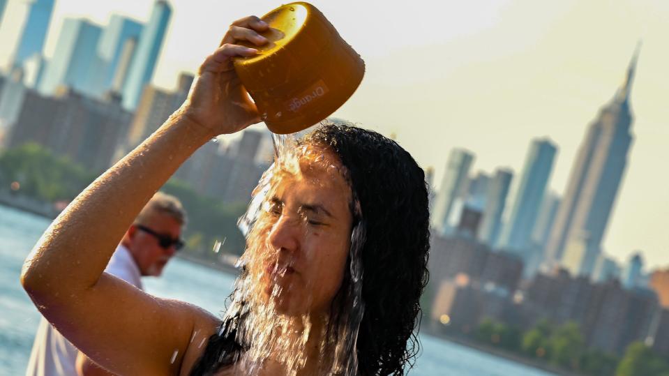 NEW YORK, NEW YORK - JULY 24: A woman pours water on her face to cool off in a fountain in Domino Park, Brooklyn with the Manhattan skyline in the background as the sun sets during a heat wave on July 24, 2022 in the Brooklyn borough of New York City. The five boroughs of New York City are under a heat advisory until 8 PM on July 24th according to the US National Weather Service. Much of the East Coast is experiencing higher than usual temperatures as a heat wave moves through the area forcing residents into parks, pools and beaches to escape the heat. (Photo by Alexi Rosenfeld/Getty Images)