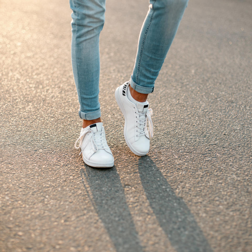 Men's legs in blue stylish jeans in white fashionable sneakers on the background of asphalt. Close-up.