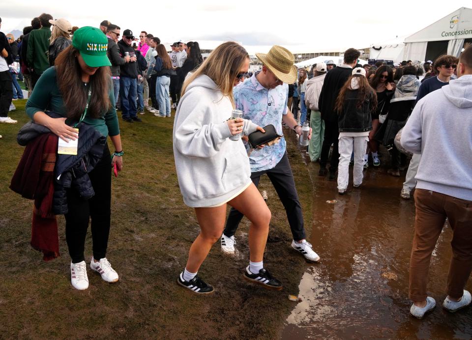 Golf fans step over the mud from the morning rain near the 10th green during the third round at the WM Phoenix Open at TPC Scottsdale on Feb. 10, 2024.