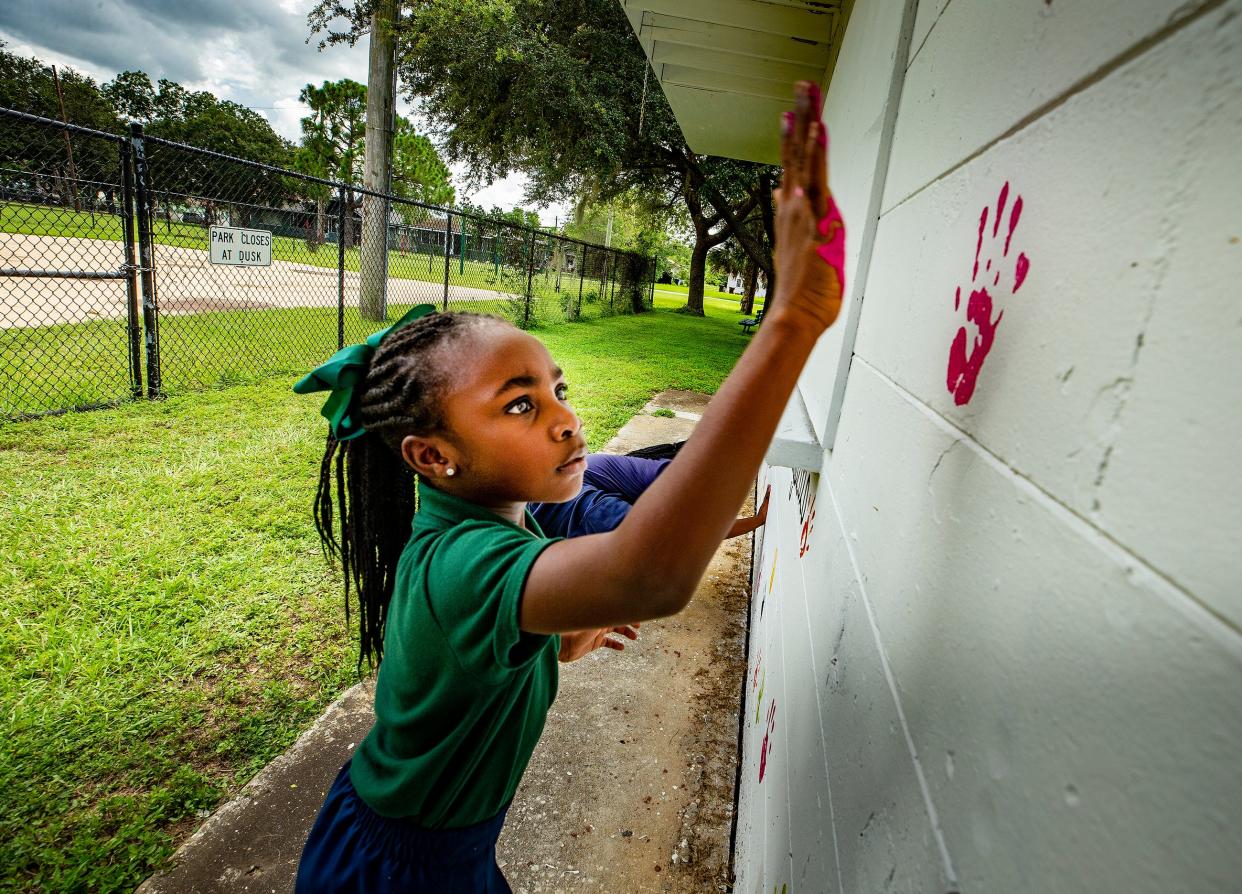 Aubrey Amos, 6, places a painted handprint on a mural wall at Spence Park In Mulberry. A nonprofit organization, Inspired Ambitious Young Believers Inc., is completing a second mural at the park. It sponsored a first mural painted by Gabriela Jaxon of Lakeland.