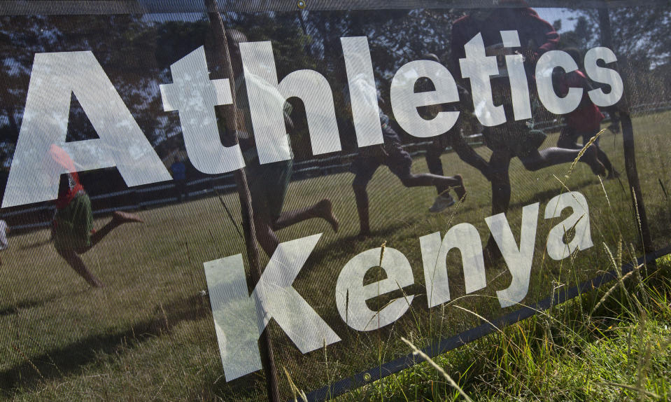 FILE - Junior athletes run past a sign for Athletics Kenya at the Discovery cross country races, an annual race held to identify up-and-coming new young talent, in Eldoret, Kenya on Jan. 31, 2016. Kenya has achieved unparalleled success in modern distance running, but a wave of positive drug tests over the last decade has ruined that reputation, made it the sport's latest doping pariah, and pushed it to the brink of a sweeping international ban that would sit it alongside Russia. (AP Photo/Ben Curtis, File)