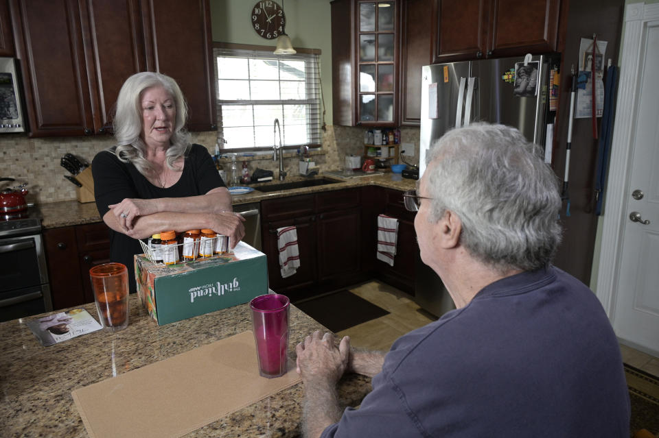 Retiree Donna Weiner, left, talks with her husband Norman Weiner at the kitchen table with the daily prescription medications that she needs and pays over $6,000 a year through a Medicare prescription drug plan at her home, Tuesday, Oct. 5, 2021, in Longwood, Fla. Weiner supports giving Medicare authority to negotiate drug prices. Negotiating Medicare drug prices is the linchpin of President Joe Biden's ambitious health care agenda. Not only would consumers see lower costs, but savings would be plowed into other priorities such as dental coverage for retirees and lower premiums for people with plans under the Obama-era health law. (AP Photo/Phelan M. Ebenhack)