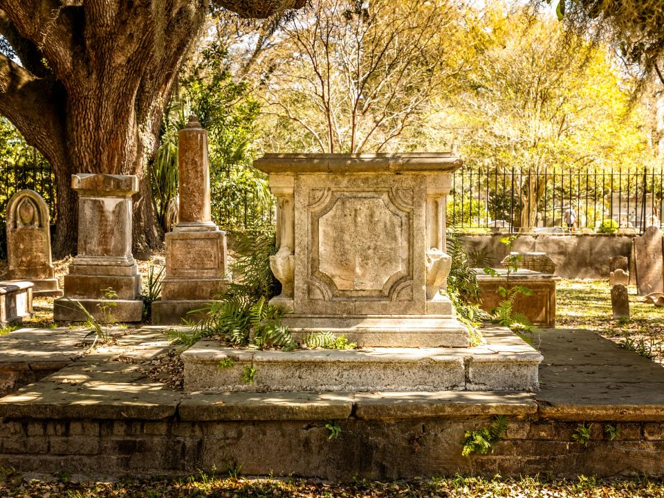 A victorian cemetery has concrete gravestones overrun by moss and plants.