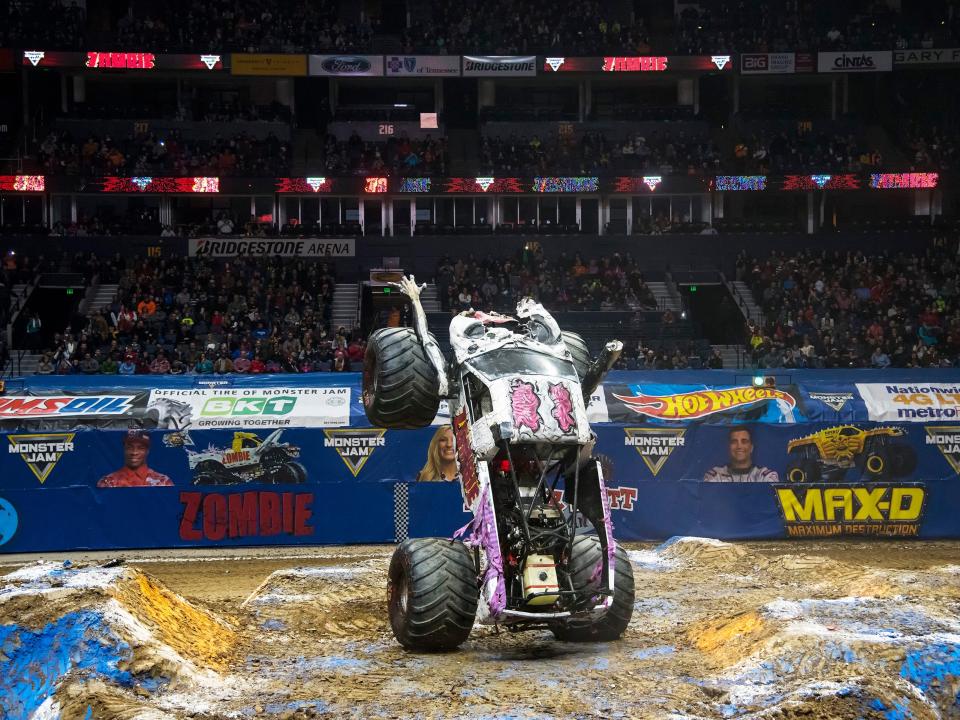 A monster truck stands on its back wheels in front of a crowd.