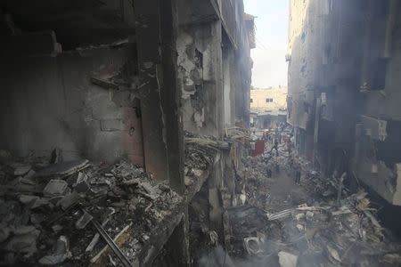 Palestinians look at damaged houses and the remains of a commercial center (L), which witnesses said was hit by an Israeli air strike on Saturday, in Rafah in the southern Gaza Strip August 24, 2014. REUTERS/Ibraheem Abu Mustafa