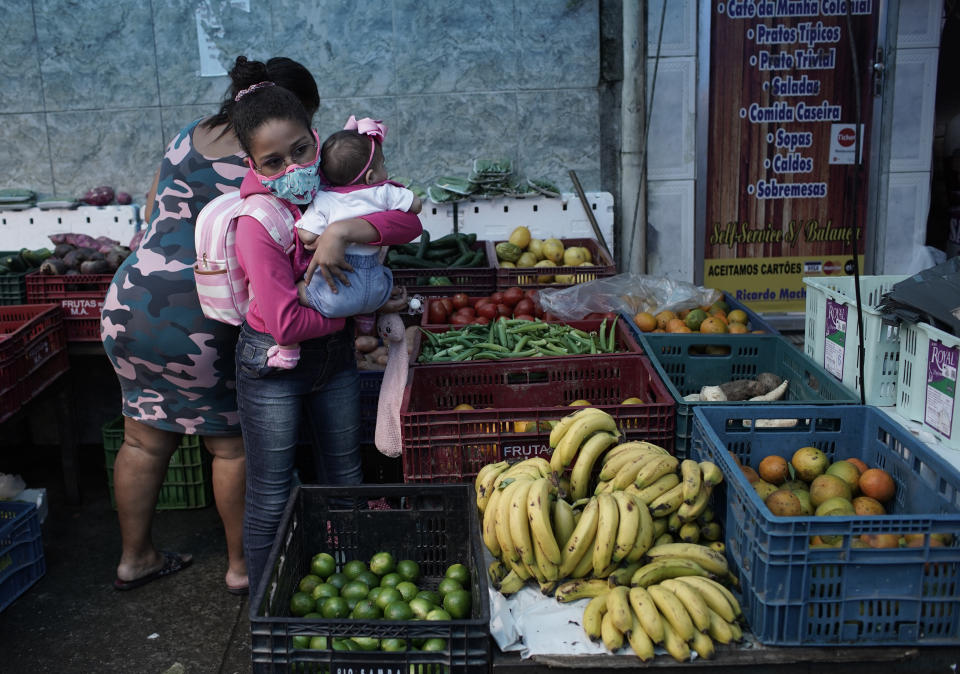 A woman carrying a baby buys fruit at a shop amid the new coronavirus pandemic in Rio de Janeiro, Brazil, Friday, Oct. 9, 2020. Many people in Brazil are struggling to cope with less pandemic aid from the government and jumping food prices, with millions expected to slip back into poverty. (AP Photo/Silvia Izquierdo)