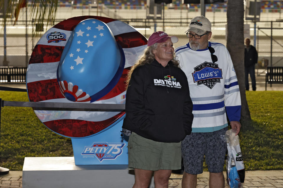 Race fans pose for a photo near a large cowboy hat honoring the Petty family for 75-years of auto racing Wednesday, Feb. 14, 2024, at Daytona International Speedway in Daytona Beach, Fla. (AP Photo/Terry Renna)