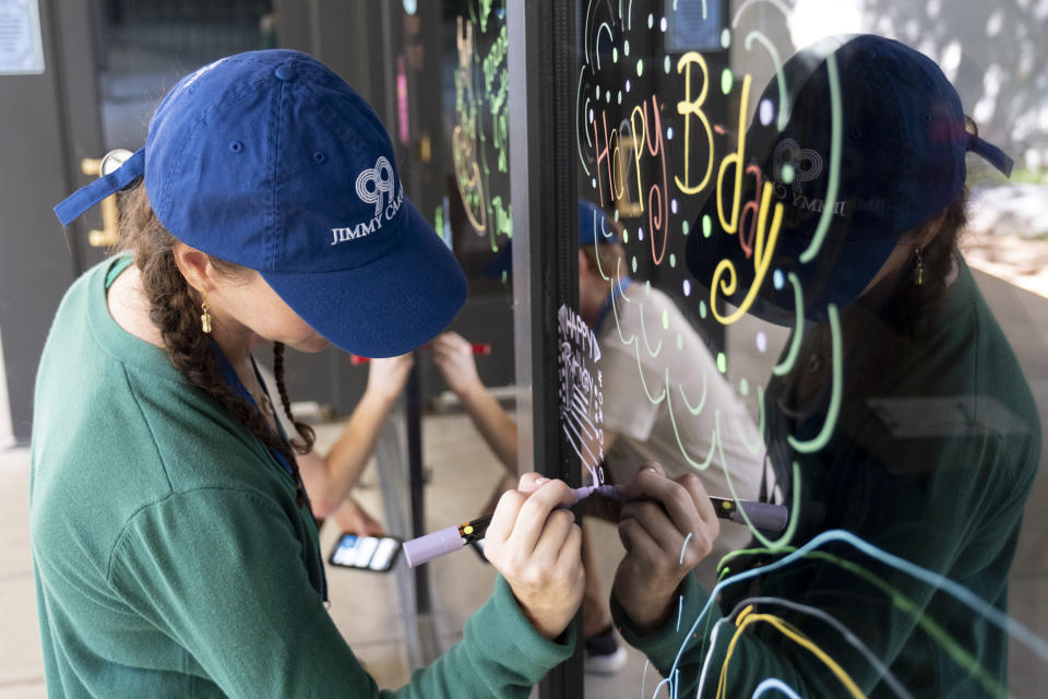 Courtney Lonsway, a volunteer at The Carter Center in Atlanta, writes birthday wishes on the center's window during a celebration for President Jimmy Carter's 99th birthday held on Saturday, Sept. 30, 2023. (AP Photo/Ben Gray)