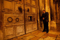 FILE PHOTO: Adeeb Joudeh (R), a Muslim, who says his family were entrusted as the custodians of the ancient key to the Church of the Holy Sepulchre, looks at a priest as he peers through an opening in the church doors as they prepare to open it, in Jerusalem's Old City November 3, 2017. REUTERS/Ronen Zvulun/File Photo