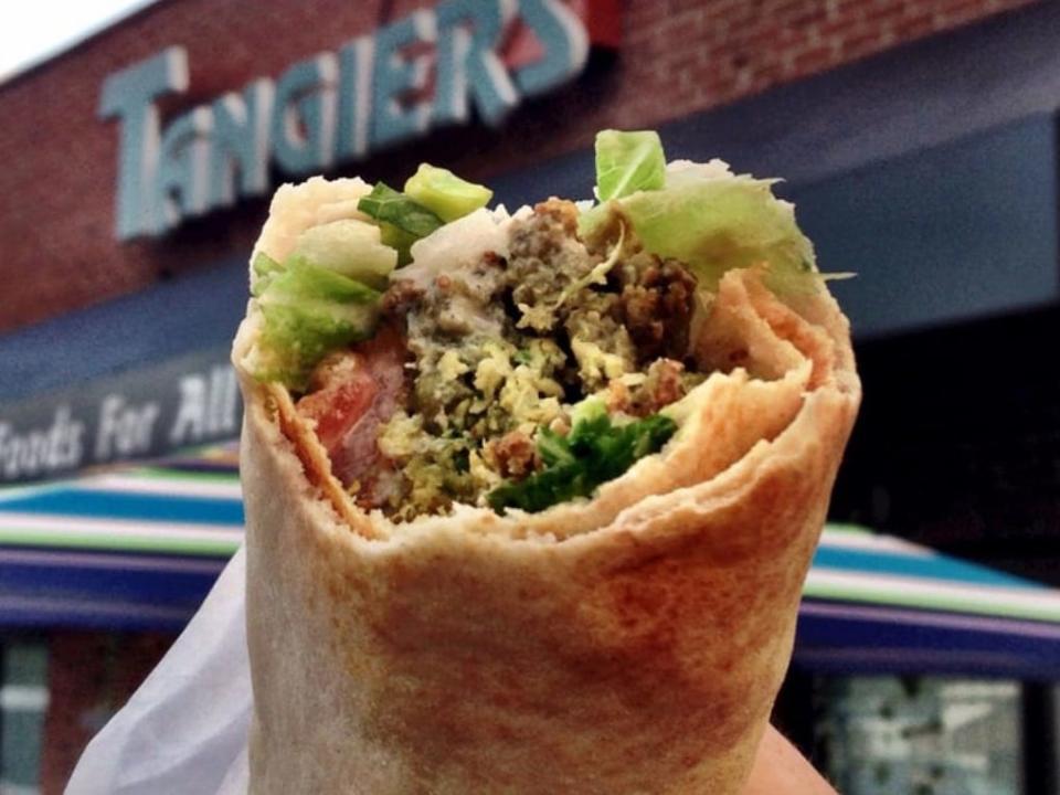 A falafel sandwich in front of a sign reading "Tangiers."