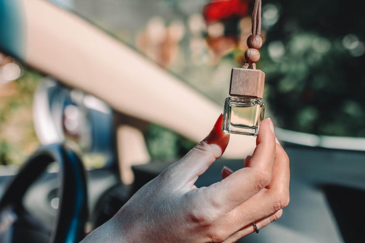 Female hand holds car air freshener. Small glass bottle with car perfume hanging in the car.