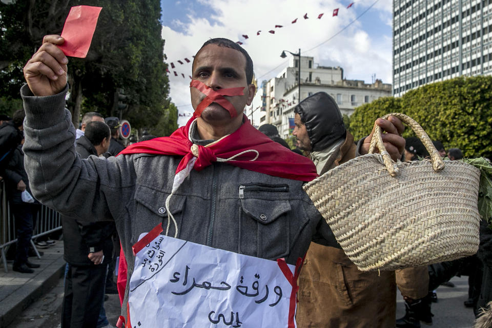 A gagged Tunisian walks with an empty basket and a red card with a poster reading "Red card to all politicians without exception" during a demonstration to mark the eighth anniversary of the democratic uprising in Tunis, Monday, Jan.14, 2019. Tunisia is marking eight years since its democratic uprising amid deepening economic troubles and simmering anger at the revolution's unfulfilled promises. (AP Photo/Hassene Dridi)