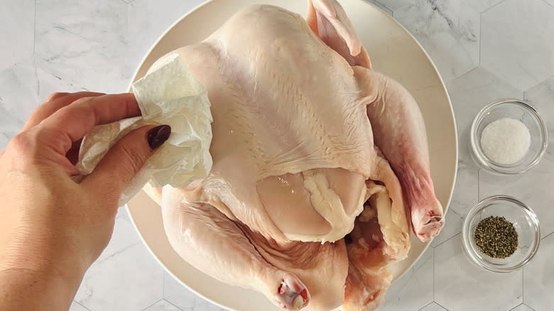 hand patting whole chicken dry with paper