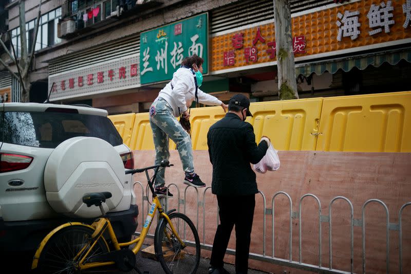 A resident pays for groceries at a residential area blocked by barriers in Wuhan