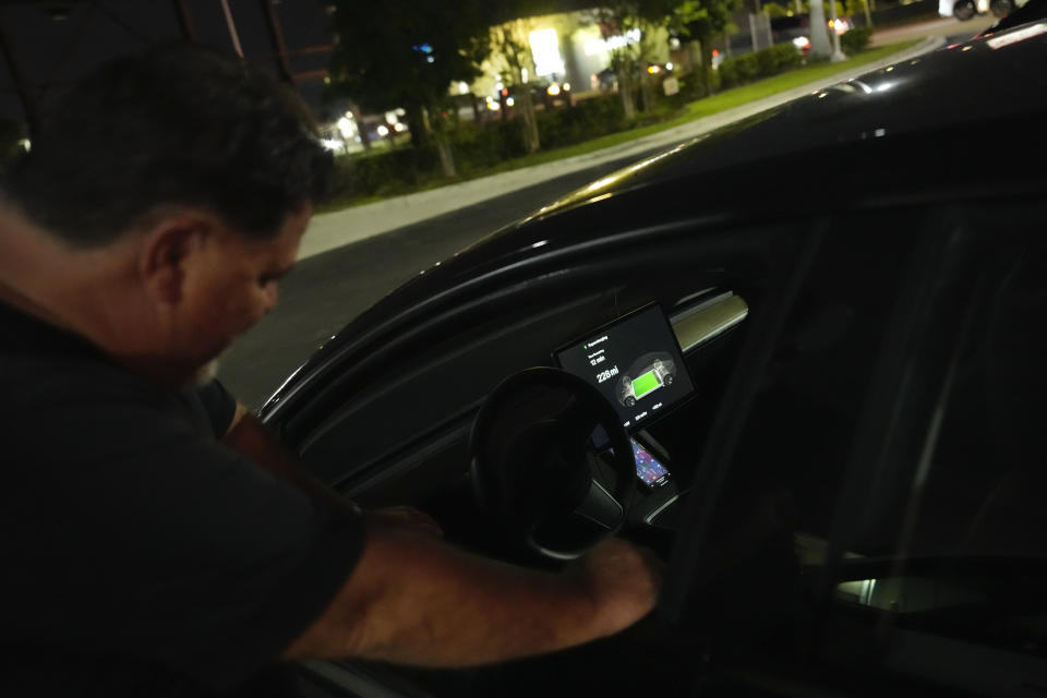 File - Uber Driver Danny Parson checks the battery level on his Tesla as it charges at a Tesla Supercharger station, Wednesday, Nov. 16, 2022, in Miami. Attacks which occurred in Florida last month sent ripples of fear among some app-based drivers, who have long demanded better protection from companies whose safety policies they say are bettered geared toward customers than workers. (AP Photo/Rebecca Blackwell, File)