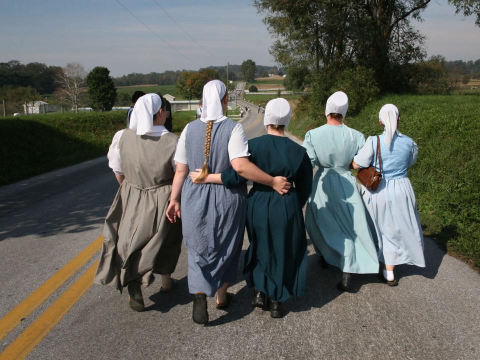 Four Amish women (and one non-Amish at far right) walk down to the Amish school (just down the hill on right, behind trees).