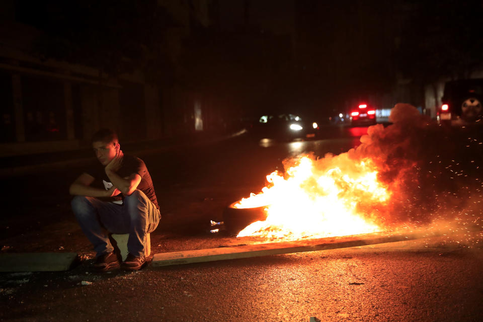 A protester sits next to burning tires, as he blocks a main street by burning tires, after a top court suspended a Central Bank decree that allowed the Lebanese to withdraw from dollar deposits at a rate two and a half times better than the fixed exchange rate, in downtown Beirut, Lebanon, early Thursday, June 3, 2021. In a late night burst of anger, dozens of protesters blocked main roads in Beirut and north of the capital to protest against the constant humiliation of Lebanese who line up to fill their cars with fuel, increasing power cuts, search for medicine and deal with confused banking decisions that are robbing thousands of their savings. (AP Photo/Hussein Malla)