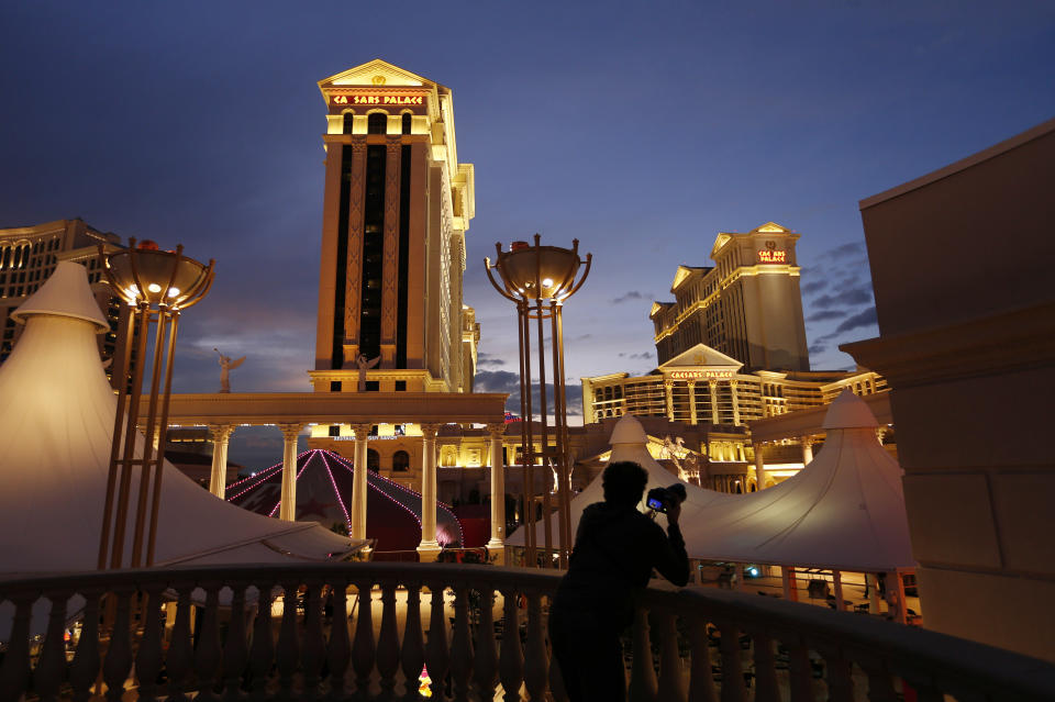 FILE - In this Jan. 12, 2015, file photo, a man takes pictures of Caesars Palace hotel and casino in Las Vegas. Reno-based Eldorado Resorts Inc. received the go-ahead from Nevada casino regulators to buy Caesars Entertainment Corp. in a $17 billion deal creating a gambling giant with properties in 16 U.S. states and several other countries. The merger won unanimous endorsement Wednesday, July 8, 2020, after pointed questions from Nevada Gaming Control Board regulators and unanimous approval from the state Gaming Commission. The Federal Trade Commission accepted the plan June 26. Approval in coming days from regulators in Indiana and New Jersey would create the world's largest casino company under the Caesars Entertainment name. (AP Photo/John Locher, File)