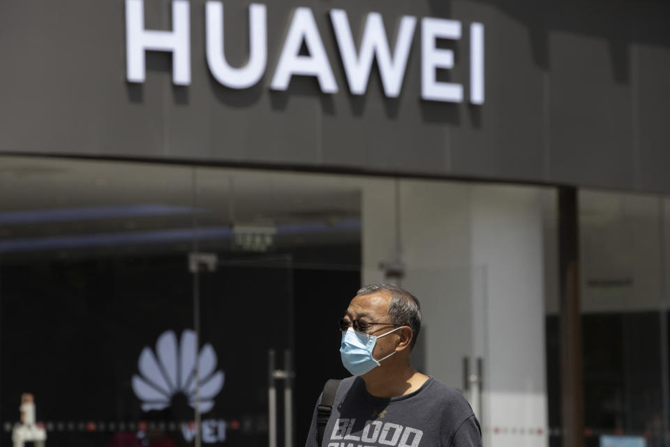 FILE - In this May 18, 2020, file photo, a man wearing a face mask to protect against the coronavirus walks past a Huawei retail store in Beijing. One of China’s biggest tech companies has criticized the Trump administration for “politicizing business” after it slapped export sanctions on 33 more Chinese enterprises and government entities. The announcement expanded a U.S. campaign against Chinese companies Washington says might be security threats or involved in human rights abuses. Beijing criticized curbs imposed earlier on tech giant Huawei and other Chinese companies but has yet to say whether it will retaliate. (AP Photo/Ng Han Guan, File)