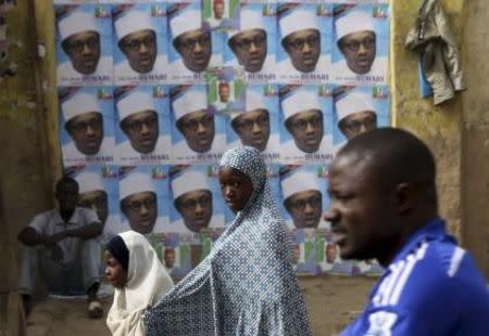 People walk in front of election posters of presidential candidate Muhammadu Buhari gestures in Kano March 27, 2015. REUTERS/Goran Tomasevic