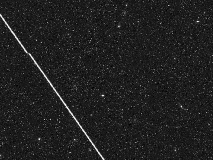 thick white satellite line streaks across black and white image of starry universe