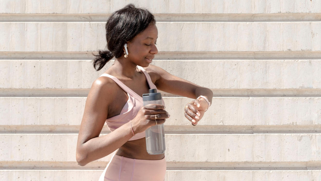  Woman with water bottle and headphones checking sports watch 