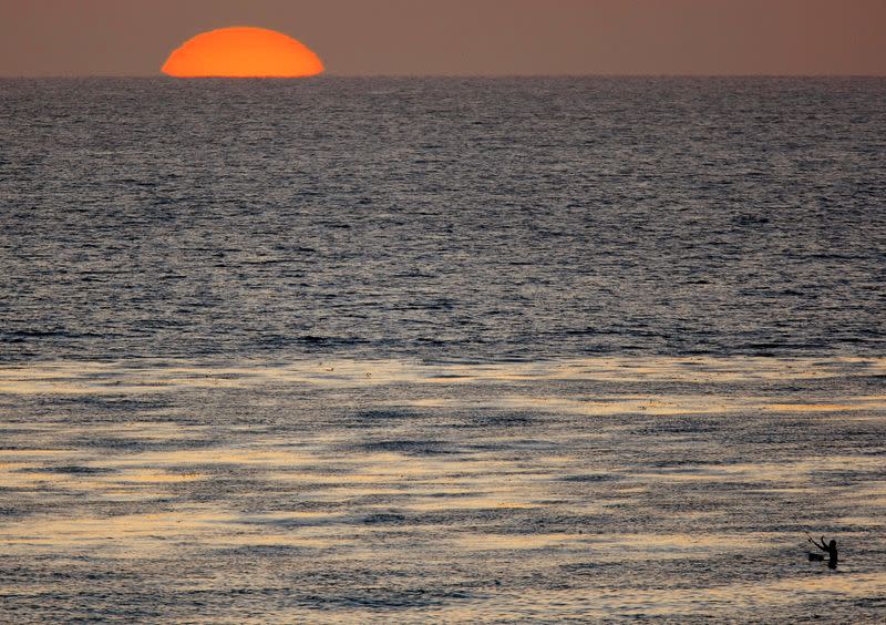 FILE PHOTO: The sun sets as a fisherman casts his line in the Pacific Ocean while sitting on a surfboard off the coast of Cardiff