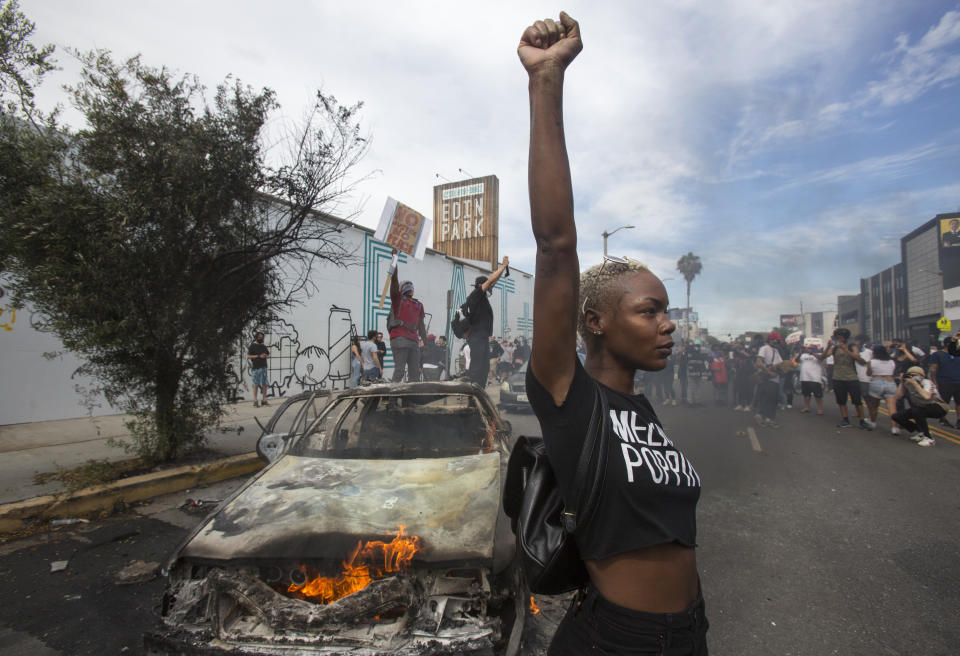 Una manifestante posa para la prensa ante un vehículo policial en llamas en Los Ángeles, el sábado 30 de mayo de 2020, durante una manifestación por la muerte de George Floyd, un hombre negro que murió tras ser detenido por la policía en Minneapolis, el 25 de mayo de 2020. (AP Foto/Ringo H.W. Chiu)