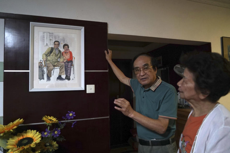 Zeng Fanzhi, a retired architect turned artist, speaks about a painting of himself and his wife as his wife, Zhao Sirong, stands beside him at their apartment in Shenzhen in southern China's Guangdong province, Friday, Oct. 27, 2023. Zeng painted stark, realist portrayals of life in China under zero-COVID, saying he did so to capture a unique moment in history. (AP Photo/Dake Kang)